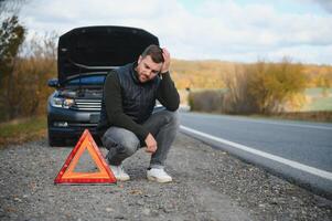 un joven hombre con un negro coche ese rompió abajo en el camino, copia espacio. foto