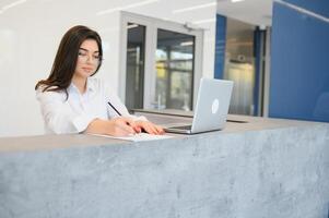 simpático joven mujer detrás el recepción escritorio administrador foto