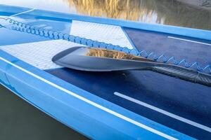 detail of stand up paddleboard with a paddle and safety leash photo