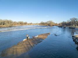 male paddler with a decked expedition canoe on a sandbar with ice floe - South Platte River in eastern Colorado photo