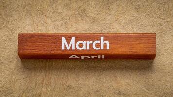 March and April text on wooden block against handmade bark paper in earth tones, calendar concept photo