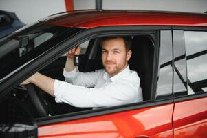 Yes, that's my new car. Customer in car dealership. Young man with keys in hand. photo