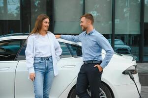 Young couple man and woman traveling together by new car having stop at charging station. photo