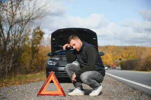 hermoso joven hombre con su coche roto abajo por el borde del camino foto