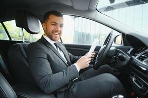 hombre de estilo y estatus. un joven apuesto con traje completo sonriendo mientras conduce un auto foto