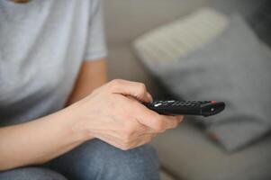 middle-aged woman sitting on the sofa and turning on the TV with a remote control. photo