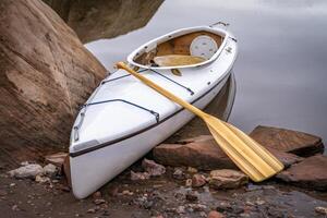 decked expedition canoe with a wooden paddle on a rocky shore of Horsetooth Reservoir near Fort Collins, Colorado, low water level fall or winter scenery photo