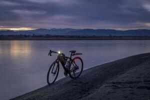 grava bicicleta en un apuntalar de un congelado lago con distante ver de rocoso montañas, invierno oscuridad en del Norte Colorado foto