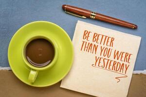 Be better than you were yesterday - motivational text on a napkin with coffee, personal development concept. photo