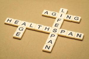 aging, lifespan and healthspan crossword in ivory letter tiles against textured handmade paper, age and longevity concept photo