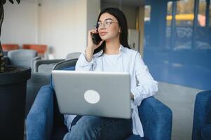 Beautiful Young Freelancer Woman Using Laptop Computer Sitting At Cafe Table. Happy Smiling Girl Working Online Or Studying And Learning While Using Notebook. Freelance Work, Business People Concept. photo