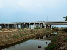 The toll road seen from the side is built on rice fields with a river beside it photo