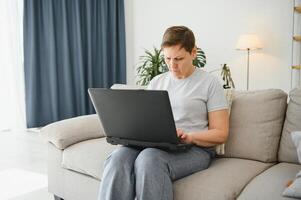 Elderly female sit on couch holding on lap laptop search information, check or typing e-mail, spend time on-line, modern tech, easy interesting pastimes services for retired older generation concept. photo