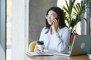 Freelance, business and e-commerce concept. Creative enthusiastic female journalist writing new article, typing on laptop, smiling, write-down project ideas, sit cafe, drink coffee working remote photo