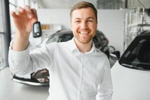 Happy buyer holding keys near the car in front of the modern avtosalon building photo