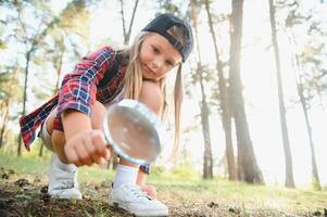 imagen de linda niño con aumentador vaso explorador el naturaleza al aire libre. adorable pequeño niña jugando en el bosque con aumentador vaso. curioso niño mirando mediante lupa en un soleado día en parque. foto