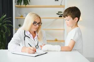 Pediatrician doctor bandaging child's arm. Broken arm in a boy. photo