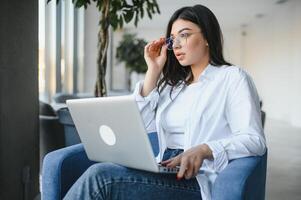 hermosa joven persona de libre dedicación mujer utilizando ordenador portátil computadora sentado a café mesa. contento sonriente niña trabajando en línea o estudiando y aprendizaje mientras utilizando cuaderno. Lanza libre trabajar, negocio personas concepto. foto