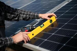 Professional worker installing solar panels on the metal construction, using different equipment, wearing helmet. Innovative solution for energy solving. Use renewable resources. Green energy. photo