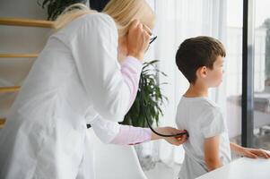 Doctor pediatrician examines child. Female doctor puts a stethoscope to a child's chest and listens to the little boy's heartbeat and lungs. Concept of health care and pediatric medical examination. photo