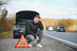 un joven hombre con un negro coche ese rompió abajo en el camino, copia espacio. foto