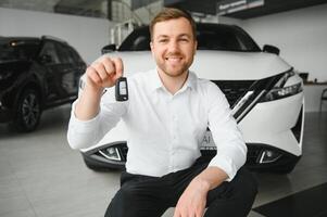 Happy buyer holding keys near the car in front of the modern avtosalon building photo