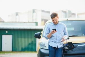 sonriente hombre desenchufar el cargador desde el coche foto