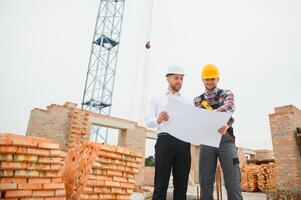 Construction engineers supervising progress of construction project stand on new concrete floor top roof and crane background. photo