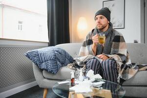 A sick man sits at home on a gray sofa with a blanket. Illness, protection, coronavirus, illness, flu photo