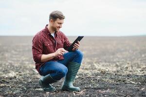 Young handsome farmer squatting in corn field in spring. Agribusiness and innovation concept photo
