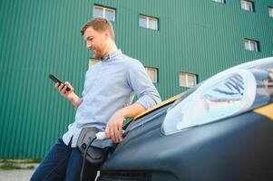 Handsome man using phone while car being charged photo