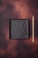 Empty black square ceramic plate on dark concrete background photo
