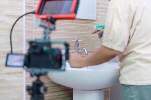 Hands of the woman uses fabric and water spray to clean the bath sink. and recording with camera photo