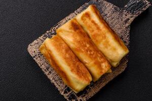 Delicious fried pancakes with filling rolled on a dark concrete background photo