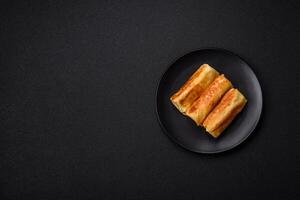 Delicious fried pancakes with filling rolled on a dark concrete background photo