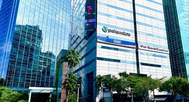 Jakarta, Indonesia - February 19th, 2024 - Tall and high glass building in front of karet sudirman bus transit in sudirman thamrin area with pohondana, bank bri, and bank capital logo banner. photo