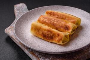 Delicious fried pancakes with filling rolled on a dark concrete background photo