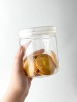 Hand holding round plain sweet bakery food biscuit treats inside clear plastic glass jar container. Object photography isolated on white studio background. photo