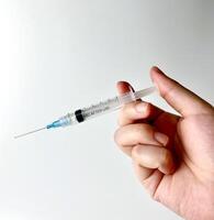 Hand holding syringe for injection with pointy needle tip photography isolated on plain white studio background. health care or medical themed image. photo