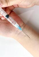 Hand holding syringe for injection. Syringe sharp pointy tip on arm skin photography isolated on plain white studio background. photo