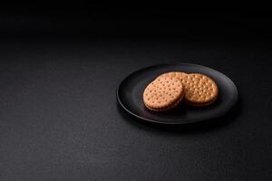 Round dotted snack snack cookies with cream on a dark concrete background photo