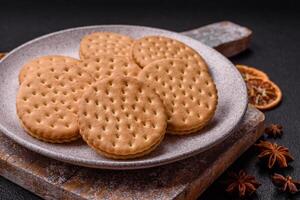 Round dotted snack snack cookies with cream on a dark concrete background photo