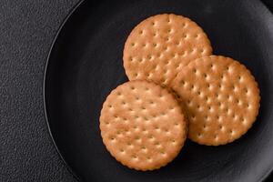 Round dotted snack snack cookies with cream on a dark concrete background photo