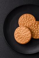 Round dotted snack snack cookies with cream on a dark concrete background photo