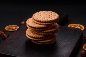 Round dotted snack snack cookies with cream on a dark concrete background photo