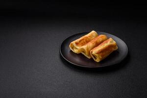 Delicious fried pancakes with filling rolled on a dark concrete background photo