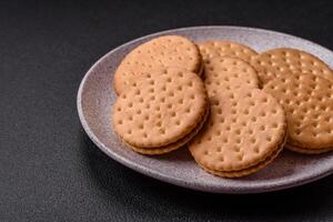 Round dotted snack snack cookies with cream on a dark concrete background photo