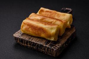 Delicious fried pancakes with filling rolled on a dark concrete background photo