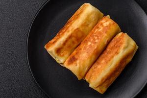 Delicious fried pancakes with filling rolled on a dark concrete background photo