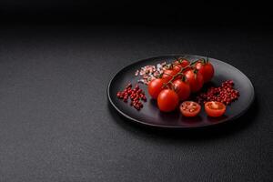 A branch of raw cherry tomatoes with salt and spices on a dark background photo
